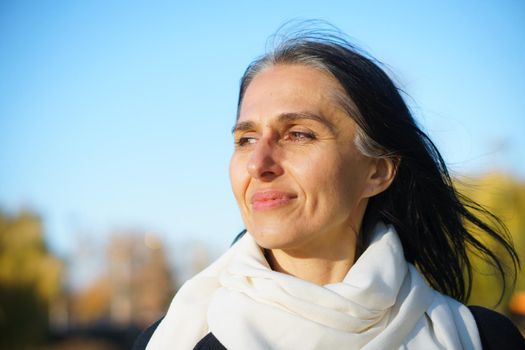 Profile side view portrait of attractive cheerful dreamy grey-haired middle-aged woman relaxing outdoors during sunny day.