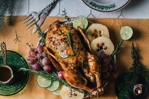 A duck baked for Thanksgiving as a symbol of family unification at a common holiday table. Still life in orange tones, shot in a light key on a white ceramic background. The atmosphere of the festival and celebration. The dish is decorated with grapes, lime, quince and aromatic herbs.