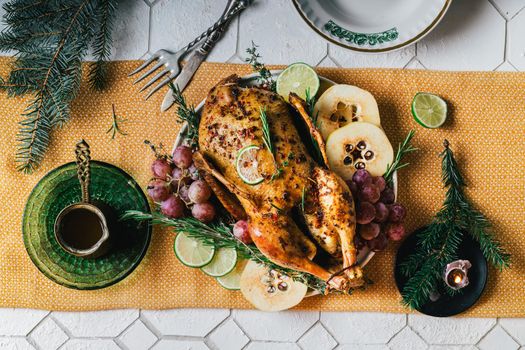 A duck baked for Thanksgiving as a symbol of family unification at a common holiday table. Still life in orange tones, shot in a light key on a white ceramic background. The atmosphere of the festival and celebration. The dish is decorated with grapes, lime, quince and aromatic herbs.