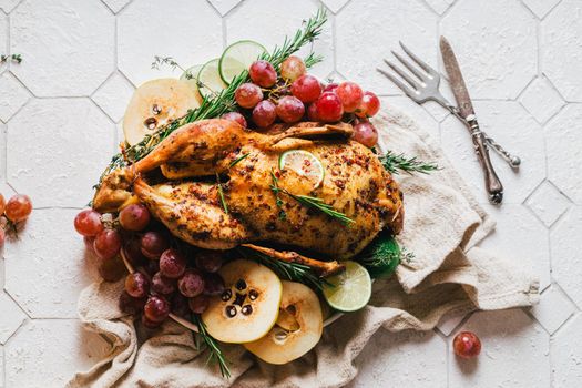 A duck baked for Thanksgiving as a symbol of family unification at a common holiday table. Still life in orange tones, shot in a light key on a white ceramic background. The atmosphere of the festival and celebration. The dish is decorated with grapes, lime, quince and aromatic herbs.