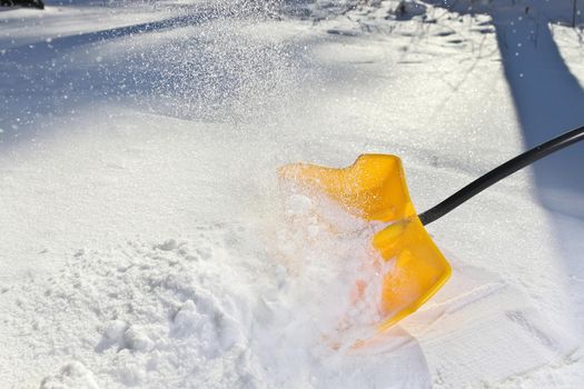 Yellow Snow Shovel Shoveling Fresh, Deep Powdery Snow on a Sunny day to Clear a Path or Driveway. High quality photo