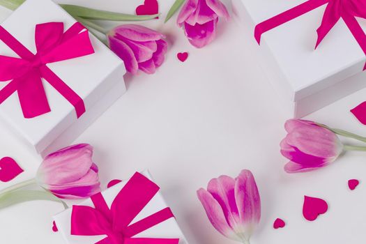 Flat lay valentines day frame of pink tulips hearts and gift boxes on a white background with copy space for text