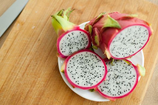 Slices of dragon fruit or pitaya with pink skin and white pulp with black seeds on white plate on the kitchen. Exotic fruits, healthy eating concept.