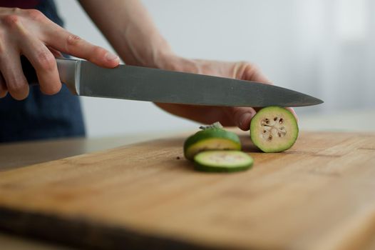 Female hands is cutting a fresh green feijoa fruit on a cut wooden board. Exotic fruits, healthy eating concept.