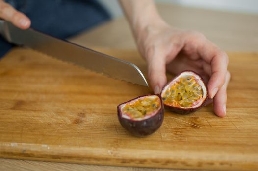 Female hands is cutting a fresh ripe passion fruit, maracuya on a cut wooden board. Exotic fruits, healthy eating concept.