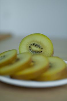 Slices of golden kiwi with yellow pulp on white plate on the kitchen. Exotic fruits, healthy eating concept.