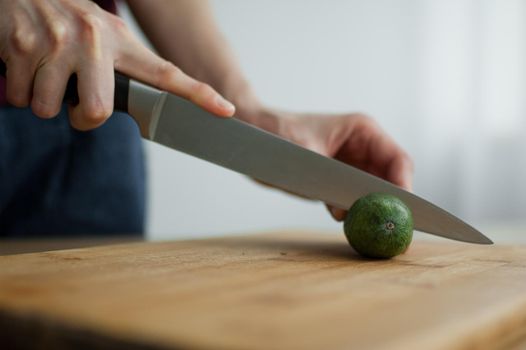 Female hands is cutting a fresh green feijoa fruit on a cut wooden board. Exotic fruits, healthy eating concept.
