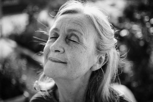 Black and white portrait of senior woman with grey hair and face with wrinkles outdoors relaxing at the park, mother's day