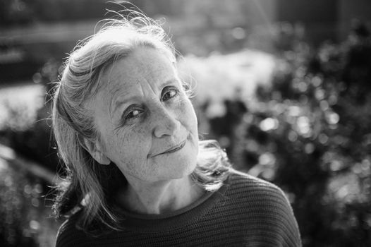 Black and white portrait of senior woman with grey hair and face with wrinkles outdoors relaxing at the park, mother's day