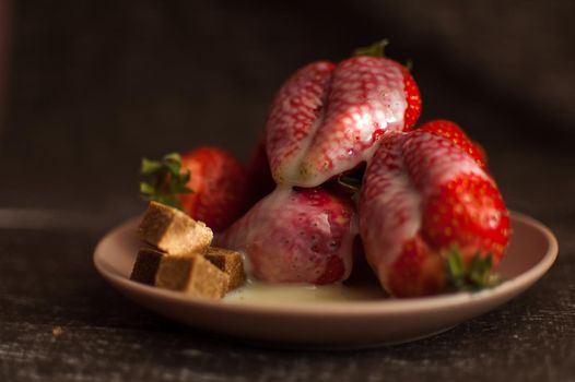 Red ripe strawberries on round plate with a few cane sugar pieces and melted white chocolate.