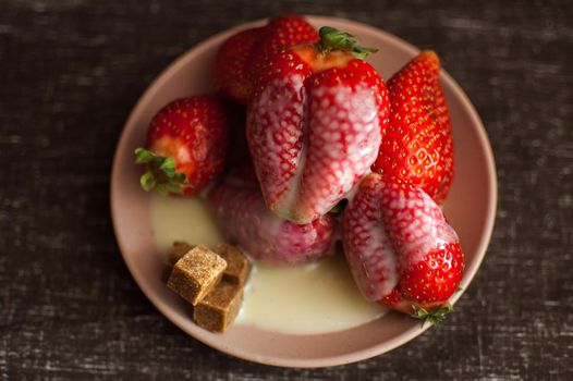 Red ripe strawberries on round plate with a few cane sugar pieces and melted white chocolate.