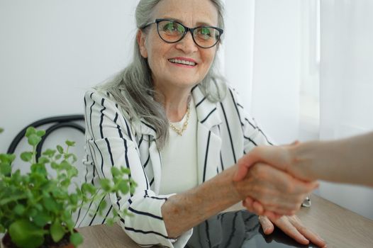 Mature businesswoman is leading an interview with new colleague and shaking their hand at the end. Business people concept.