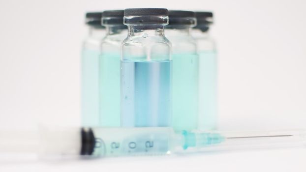 Vial vaccine, glass ampoules with transparent and blue liquid, a syringe is lying near on white background, global vaccination concept.