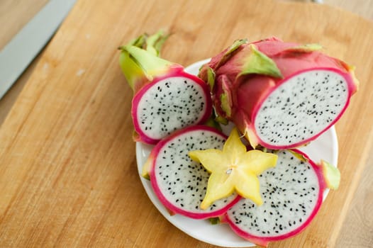 Slices of dragon fruit or pitaya with white pulp and black seeds on white plate with one slice of starfruit or averrhoa carambola. Exotic fruits, healthy eating concept.