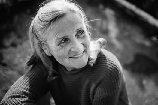 Black and white portrait of senior woman with grey hair and face with wrinkles outdoors relaxing at the park, mother's day