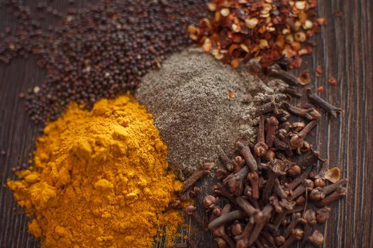 Sorted spices on dark wood background, seasonings for food. Top view of curry, paprika, pepper, cloves, bay leaf, turmeric, spices concept