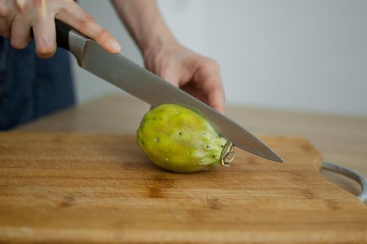 Female hands is cutting a fresh ripe cactus pear on a cut wooden board. Exotic fruits, healthy eating concept