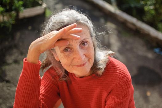 Close up face of happy senior woman with grey hair looking at camera while spending time outdoors during sunny day, retirement concept