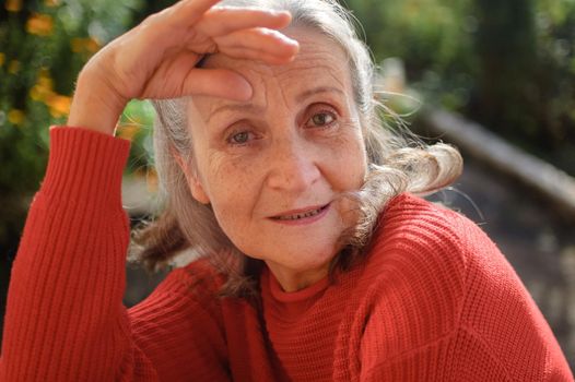 Close up portrait of a smiling senior woman with grey hair and face with wrinkles outdoors relaxing at park during sunny day, mothers day