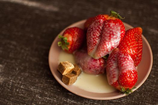 Red ripe strawberries on round plate with a few cane sugar pieces and melted white chocolate.