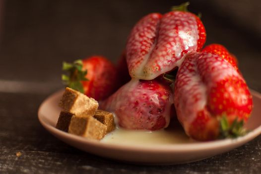Red ripe strawberries on round plate with a few cane sugar pieces and melted white chocolate.