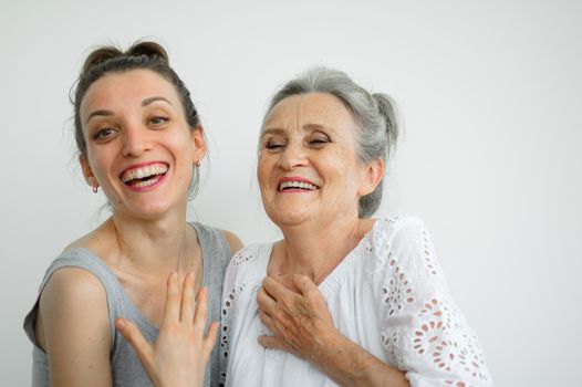 Happy senior mother is hugging her adult daughter, the women are laughing together, sincere family of different age generations having fun on white background, mothers day