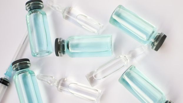 Vial vaccine, top view of glass ampoules with transparent and blue liquid lying on white background, global vaccination concept.