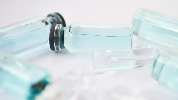 Vial vaccine, top view of glass ampoules with transparent and blue liquid lying on white background, global vaccination concept.