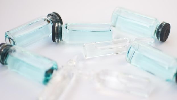 Vial vaccine, top view of glass ampoules with transparent and blue liquid lying on white background, global vaccination concept.