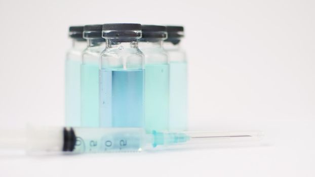 Vial vaccine, glass ampoules with transparent and blue liquid, a syringe is lying near on white background, global vaccination concept.