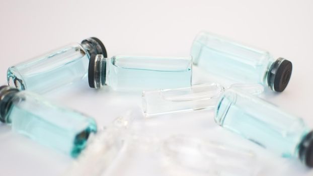 Vial vaccine, top view of glass ampoules with transparent and blue liquid lying on white background, global vaccination concept.