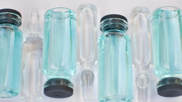 Vial vaccine, top view of glass ampoules with transparent and blue liquid lying on white background, global vaccination concept.