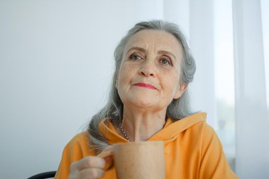 Elderly gray-haired woman is drinking coffee while sitting at home. Happy retirement.