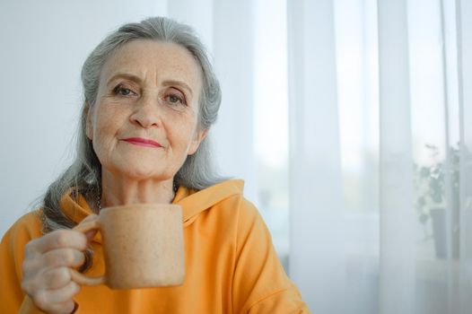 Happy vivacious middle-aged blond woman holding a cup of tea or coffee looking at the camera with a beaming warm smile.