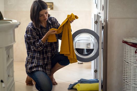 A young girl puts things in the washing machine, a woman sits on the floor of a cozy house and looks at the stain on her jacket, which needs to be removed with detergent.