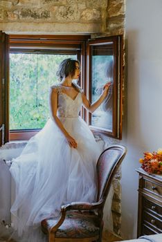 Artistic processing Fantasy girl princess in WHITE WEDDING dress stands in medieval CASTLE room looking vintage window. Bride in a luxury apartment in a wedding dress.. Sweet and gentle girl with fair skin alone in silence in an old castle, spirit of abandoned medieval building whirls in white smoke and magical thick fog in rays of sun