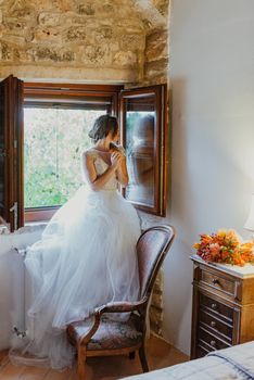 Artistic processing Fantasy girl princess in WHITE WEDDING dress stands in medieval CASTLE room looking vintage window. Bride in a luxury apartment in a wedding dress.. Sweet and gentle girl with fair skin alone in silence in an old castle, spirit of abandoned medieval building whirls in white smoke and magical thick fog in rays of sun