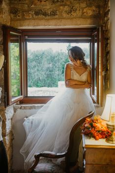 Artistic processing Fantasy girl princess in WHITE WEDDING dress stands in medieval CASTLE room looking vintage window. Bride in a luxury apartment in a wedding dress.. Sweet and gentle girl with fair skin alone in silence in an old castle, spirit of abandoned medieval building whirls in white smoke and magical thick fog in rays of sun