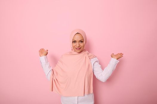 Young beautiful Muslim Arabic woman in pink hijab over isolated pink background holding a copy space imaginary on the palm to insert an advertising