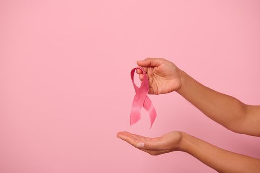 Close-up of woman's hands holding a pink ribbon, symbol of World Breast Cancer awareness Day, 1 st October. Woman's health and medical concept, national Cancer Survivor Day, isolated with copy space