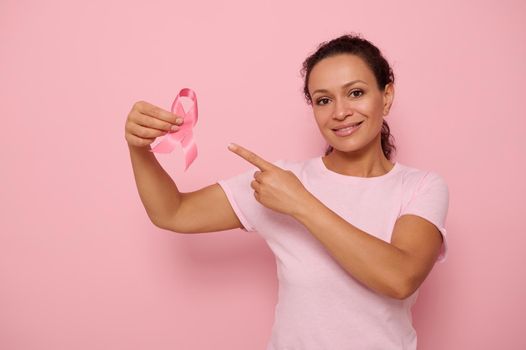 Cute Hispanic woman holding a pink ribbon, symbol of World Breast Cancer awareness Day, in 1 st October. Woman's health care concept, October Pink day, World Cancer Day, national Cancer Survivor Day.
