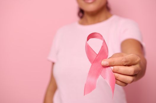 Close-up. Hand of woman in pink t-shirt, holding pink ribbon. World Cancer Day. Breast and abdominal cancer awareness, October Pink day on colored background, copy space. Breast cancer support concept