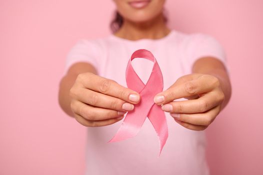 Cropped view of a young woman in pink t-shirt holding a pink satin ribbon isolated on colored background with copy space. International Breast Cancer awareness Day, Breast cancer support concept.