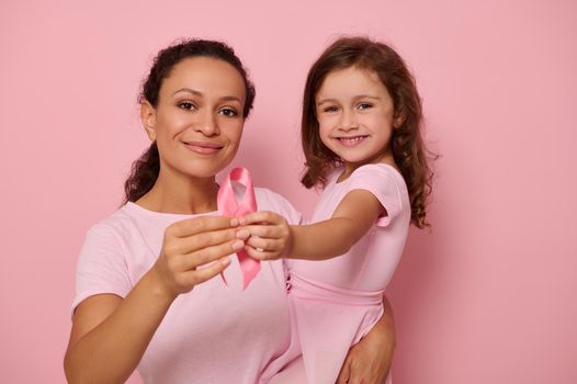 Two generations of women, mom and daughter hugging each other, holding pink ribbon, Breast Cancer Awareness Day symbol, showing support and solidarity to cancer patients and survivors. Women's health