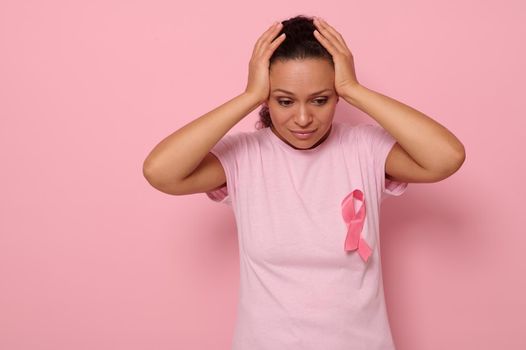 October Breast Cancer Awareness month, Woman in pink T- shirt with Pink Ribbon for supporting people living and illness, holding hands on head, isolated on pink background with copy space