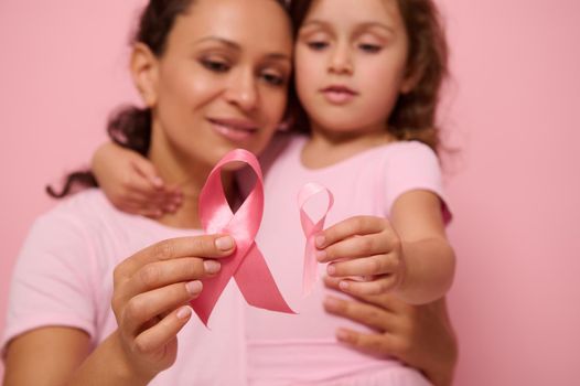 Close-up of a pink satin ribbons on blurred woman and girl hugging each other. World Breast Cancer awareness Day, 1 st October. Women's health, medical concept, World Cancer Day, Cancer Survivor Day.