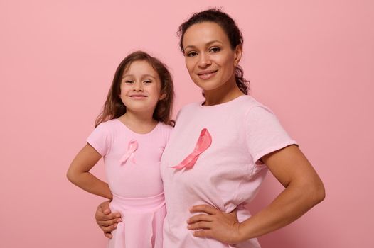 Gorgeous women of two generations, African American lady and European baby girl, in pink clothes and pink ribbon, support cancer survivors. Medical Concept October 1. World Breast Cancer Awareness Day