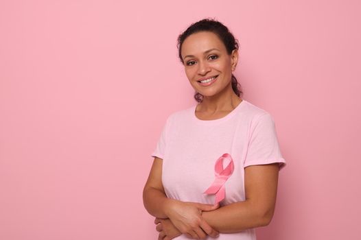 Portrait of an altruist, smiling mixed race woman in a pink T-shirt with a pink satin ribbon, symbol of International Breast Cancer Day. Educational program for the fight against cancer. 1 October