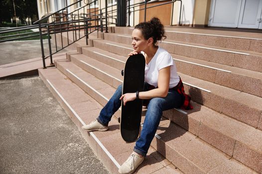 Portrait of beautiful young african american woman with skateboard sitting on steps of unrecognizable building