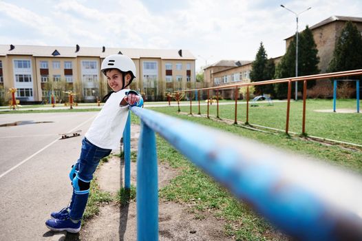Full length handsome boy in safety helmet and protective gear leaning on horizontal bar on playground outdoors. Concept of leisure activity, sport, extreme, hobby.